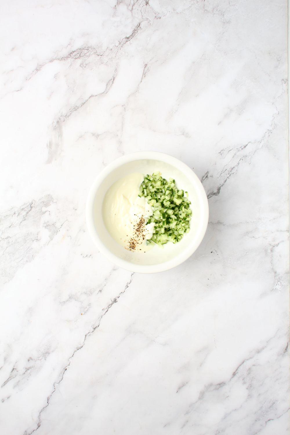 Combining yogurt, lemon juice, diced cucumber, and minced garlic in a bowl